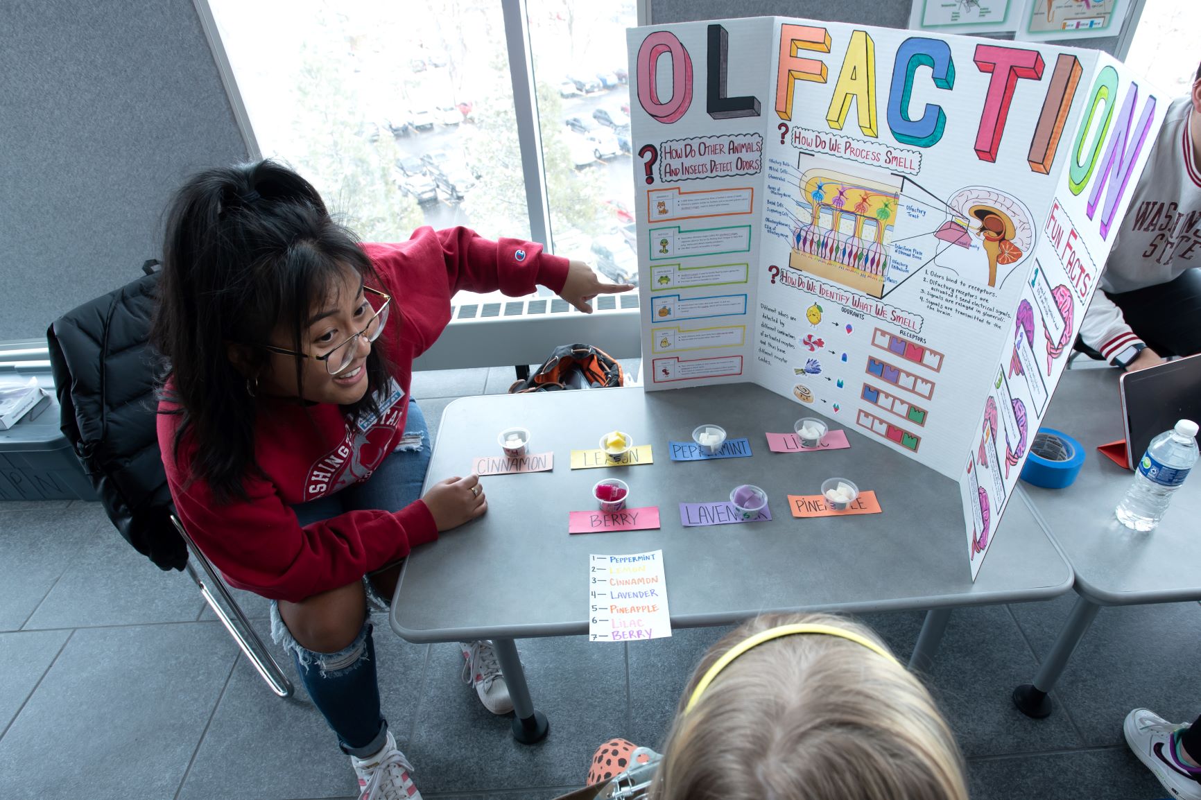 WSU student leans forward to welcome a elementary school student to their table at the Neuroscience Fair.
