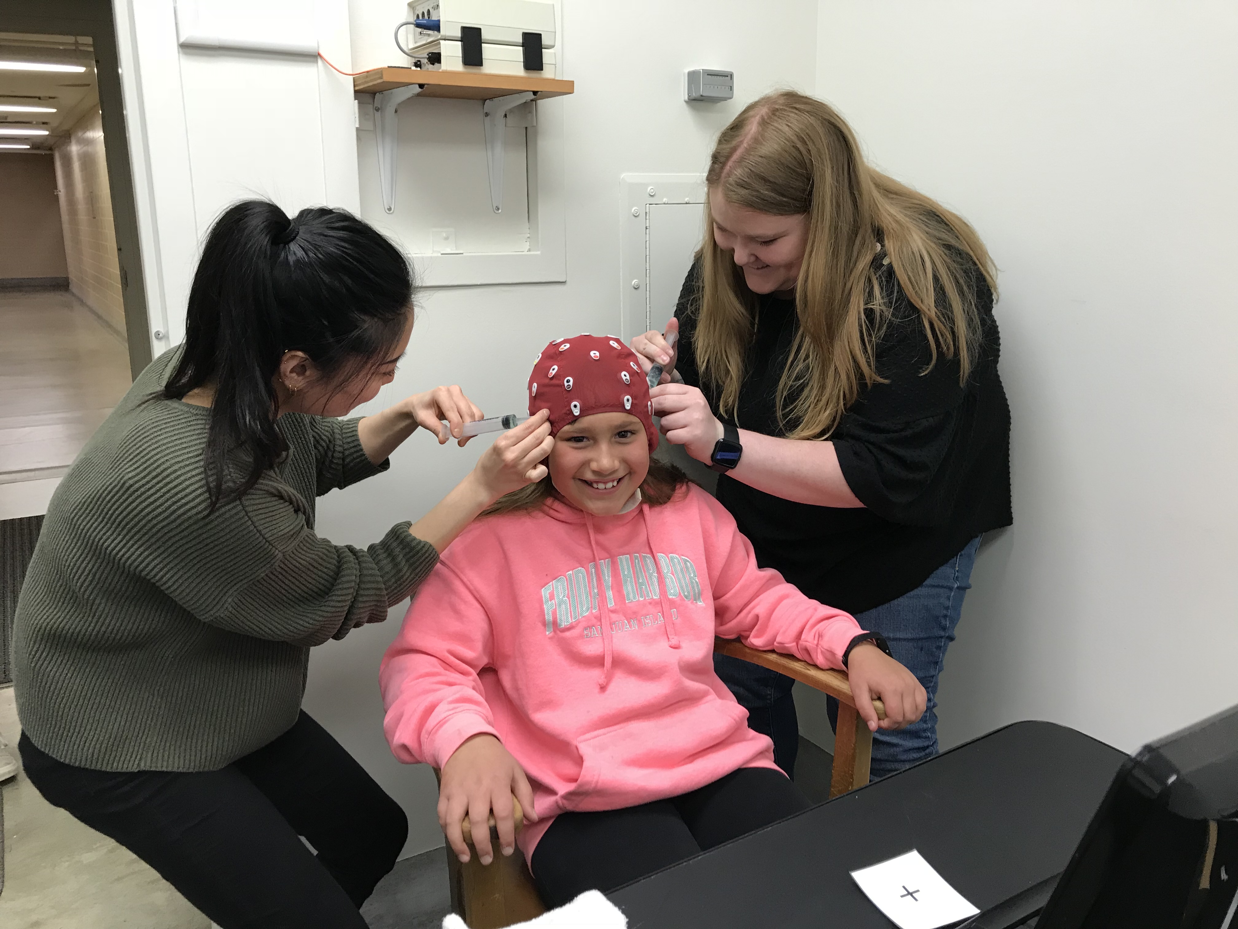 Students helping a younger student put on a brain cap for human development research